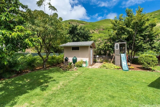 view of yard with a playground, fence, a shed, an outdoor structure, and a mountain view