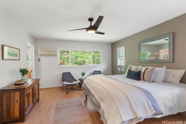 bedroom featuring a ceiling fan, light wood-style floors, and a wall mounted air conditioner