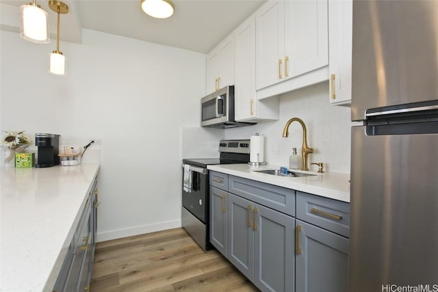 kitchen with light wood-style flooring, a sink, stainless steel appliances, white cabinets, and light countertops