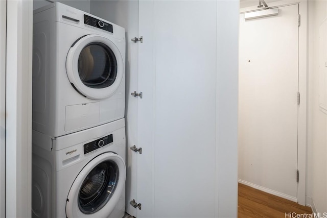 clothes washing area with stacked washer and dryer, wood finished floors, and laundry area