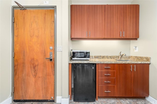 kitchen featuring refrigerator, light stone counters, brown cabinets, and a sink