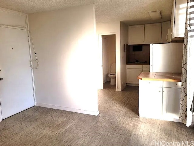 kitchen with freestanding refrigerator, a sink, tile counters, light wood-style floors, and a textured ceiling