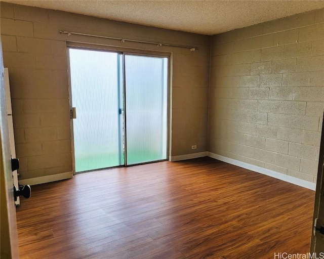 spare room with concrete block wall, dark wood-style floors, and a textured ceiling