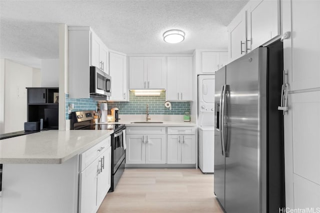 kitchen with a sink, light countertops, stacked washer / drying machine, white cabinetry, and stainless steel appliances