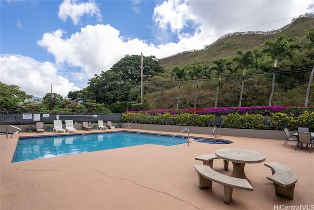 pool with a patio area, a hot tub, a mountain view, and fence