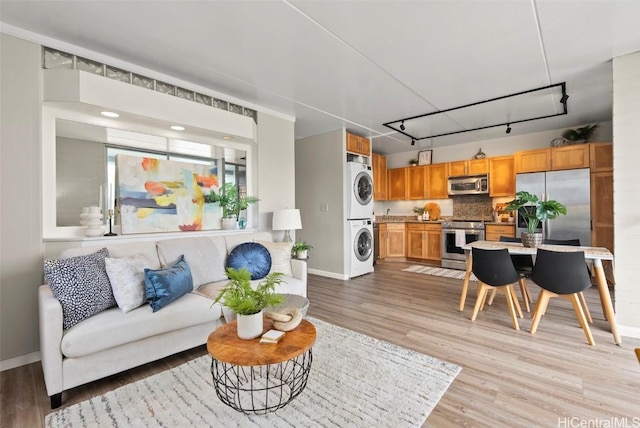 living area featuring stacked washer / dryer, rail lighting, baseboards, and light wood finished floors