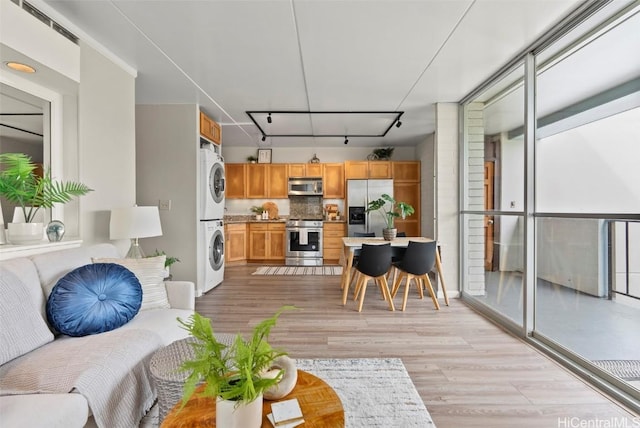 living room with light wood-type flooring, stacked washer / drying machine, rail lighting, and expansive windows