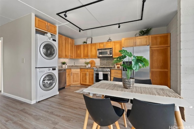 kitchen featuring stacked washer and dryer, light wood-style flooring, appliances with stainless steel finishes, light countertops, and decorative backsplash