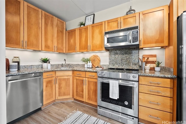 kitchen with light stone countertops, a sink, stainless steel appliances, light wood-style floors, and backsplash