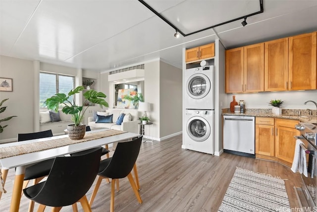 kitchen featuring light wood finished floors, light stone counters, stacked washer and clothes dryer, stove, and stainless steel dishwasher