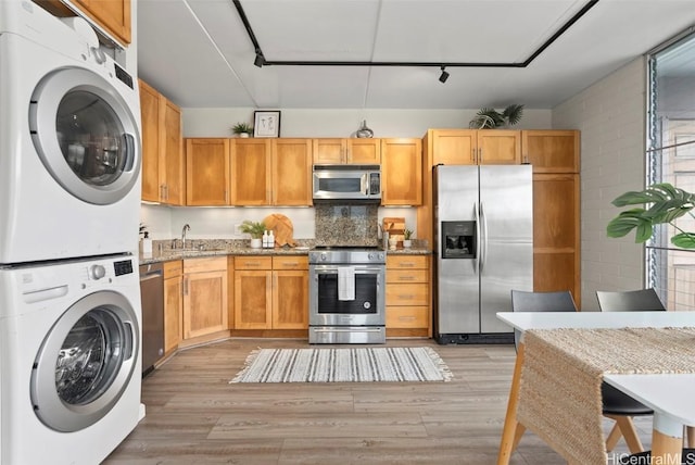 kitchen featuring light wood-style flooring, appliances with stainless steel finishes, stacked washer / drying machine, and a sink