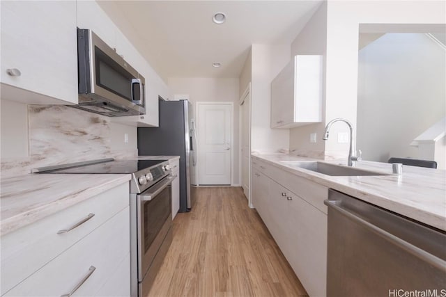 kitchen featuring a sink, decorative backsplash, stainless steel appliances, white cabinets, and light wood-style floors