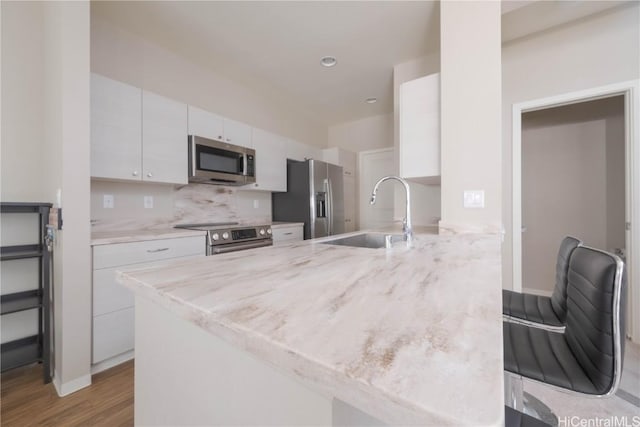 kitchen with decorative backsplash, appliances with stainless steel finishes, a peninsula, white cabinetry, and a sink