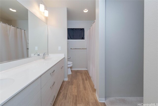 full bath featuring wood finished floors, baseboards, double vanity, a sink, and toilet