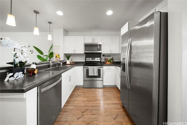 kitchen with light wood-style flooring, a sink, dark countertops, white cabinetry, and appliances with stainless steel finishes