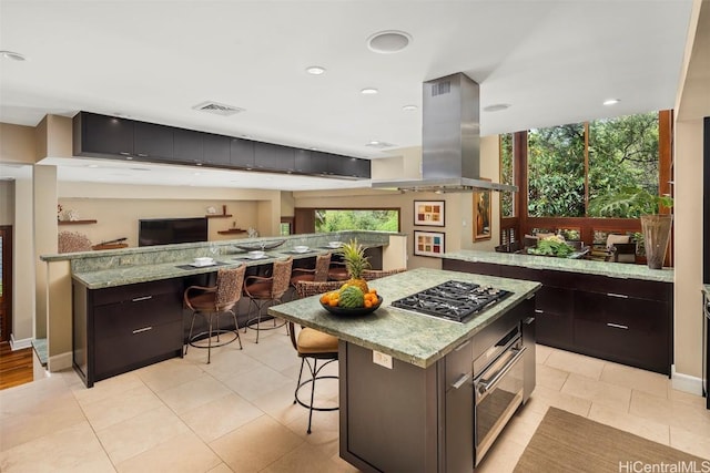 kitchen featuring light stone counters, visible vents, a breakfast bar, stainless steel gas stovetop, and island range hood