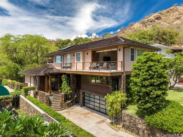 view of front of home with a balcony, driveway, an attached garage, stucco siding, and stone siding