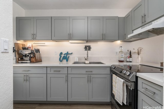 kitchen with gray cabinets, under cabinet range hood, a sink, stainless steel range with electric cooktop, and light countertops