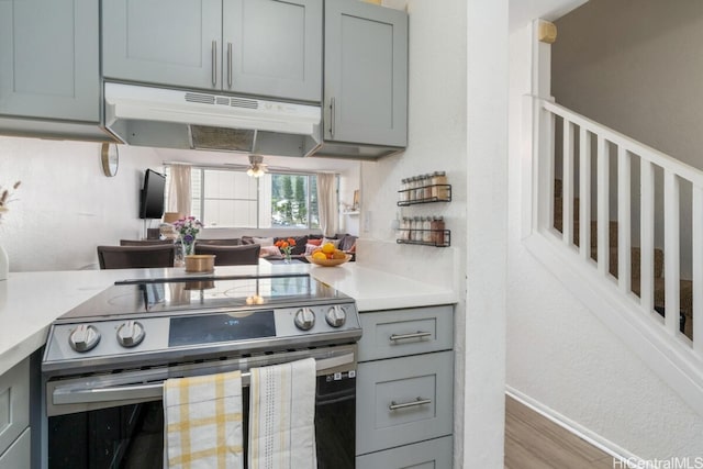 kitchen featuring gray cabinetry, under cabinet range hood, light countertops, stainless steel range with electric stovetop, and wood finished floors