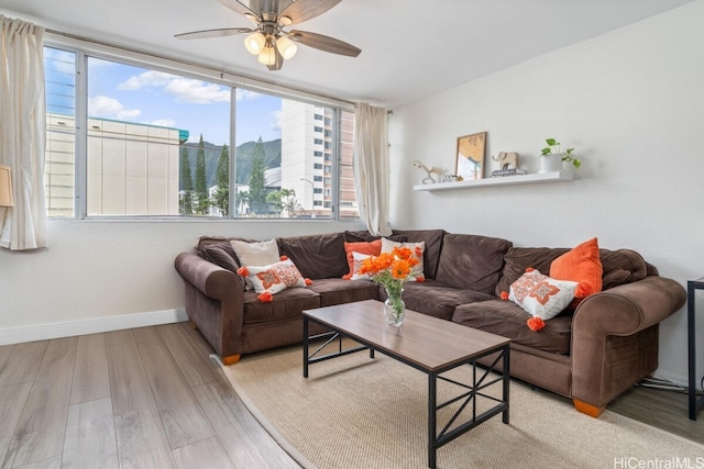 living area featuring light wood-style flooring, a ceiling fan, and baseboards