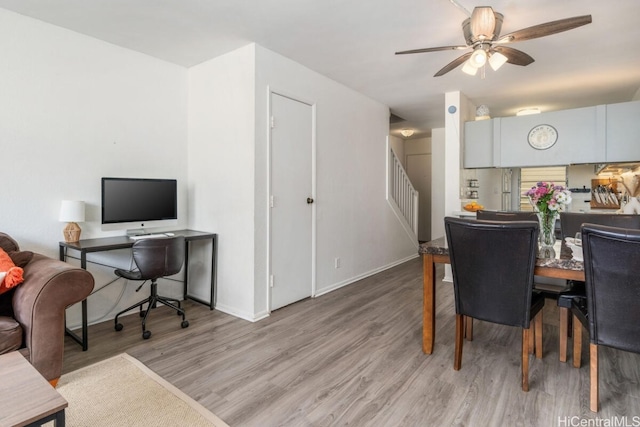 dining room with baseboards, a ceiling fan, light wood-style flooring, and stairs