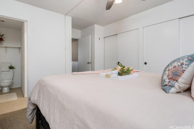 carpeted bedroom featuring multiple closets, a textured ceiling, ensuite bath, and ceiling fan