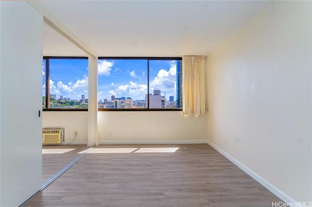 unfurnished room featuring a view of city, wood finished floors, baseboards, and a wall mounted air conditioner