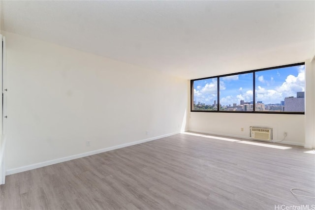 unfurnished room with baseboards, a city view, wood finished floors, and a wall unit AC