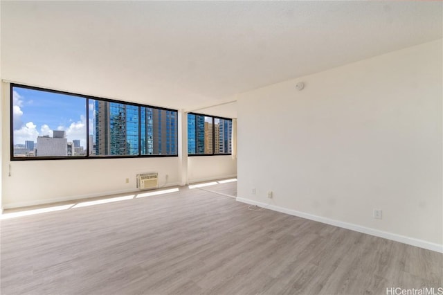 spare room with a city view, light wood-style flooring, a wall mounted AC, and baseboards