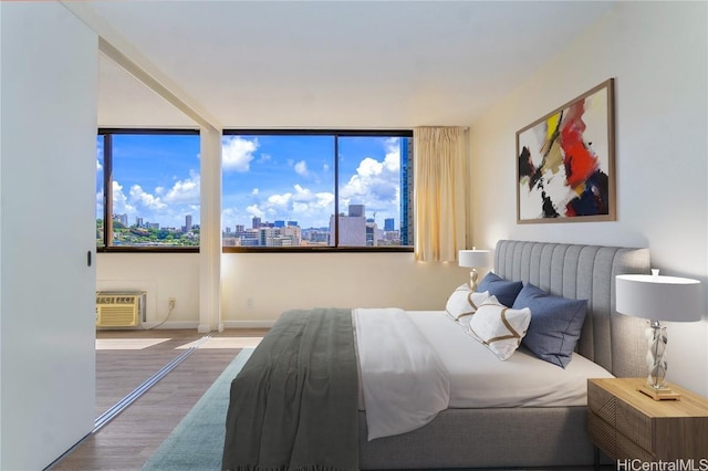 bedroom with a wall mounted air conditioner, a view of city, and wood finished floors