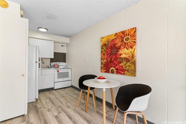 kitchen featuring light countertops, a textured ceiling, light wood-style flooring, white appliances, and tile walls