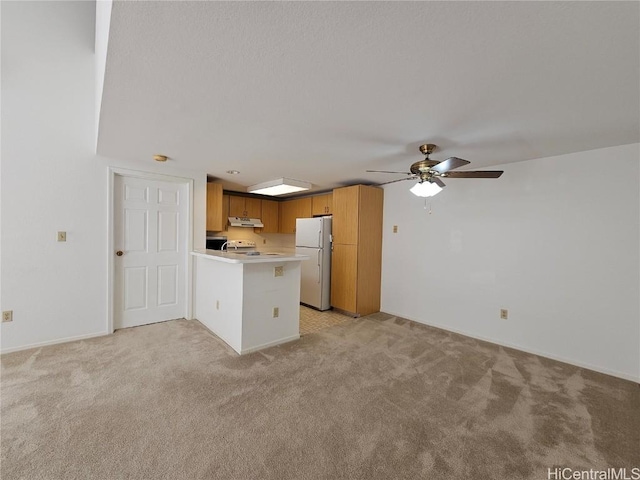 kitchen featuring a peninsula, freestanding refrigerator, light countertops, under cabinet range hood, and light carpet