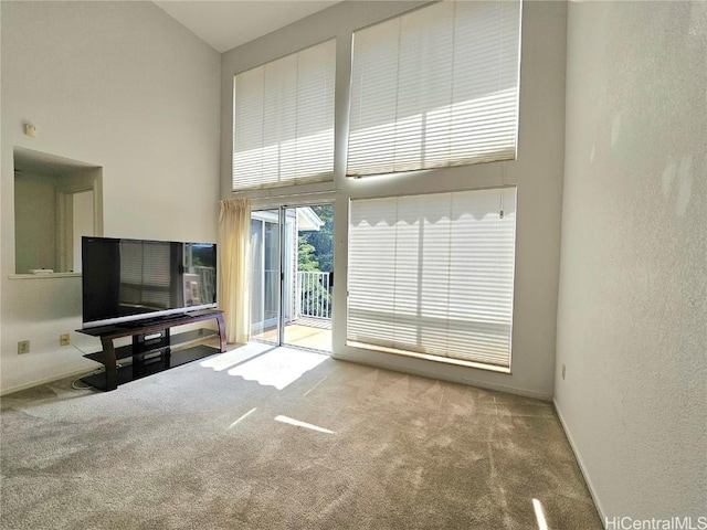 unfurnished living room with carpet flooring, a textured wall, baseboards, and a towering ceiling