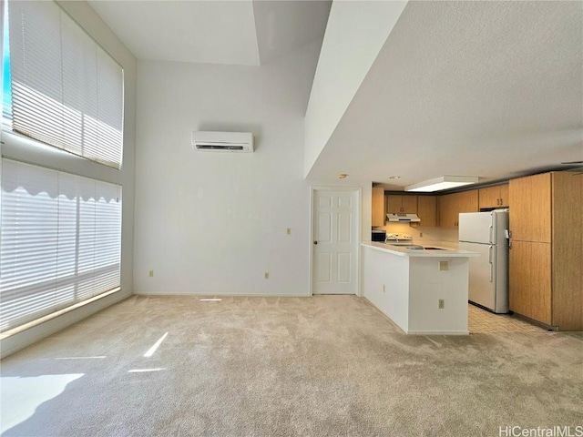 kitchen featuring a wall mounted AC, under cabinet range hood, freestanding refrigerator, a peninsula, and light colored carpet