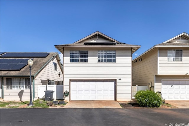 view of front of property featuring roof mounted solar panels, driveway, an attached garage, and fence