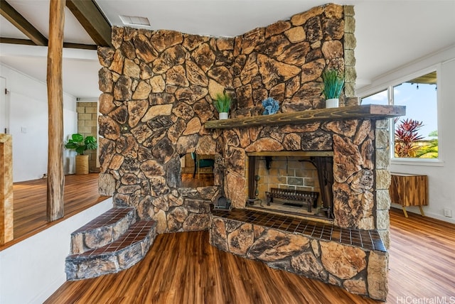 interior space with a stone fireplace, beam ceiling, wood finished floors, and visible vents