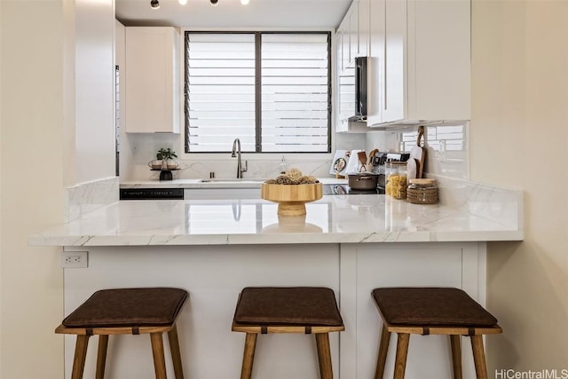 kitchen featuring a peninsula, white cabinets, light stone counters, and a sink