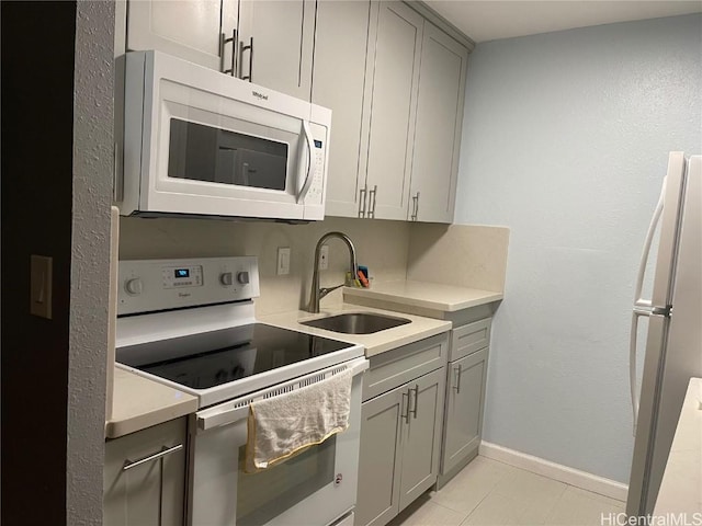 kitchen featuring baseboards, light countertops, gray cabinets, white appliances, and a sink