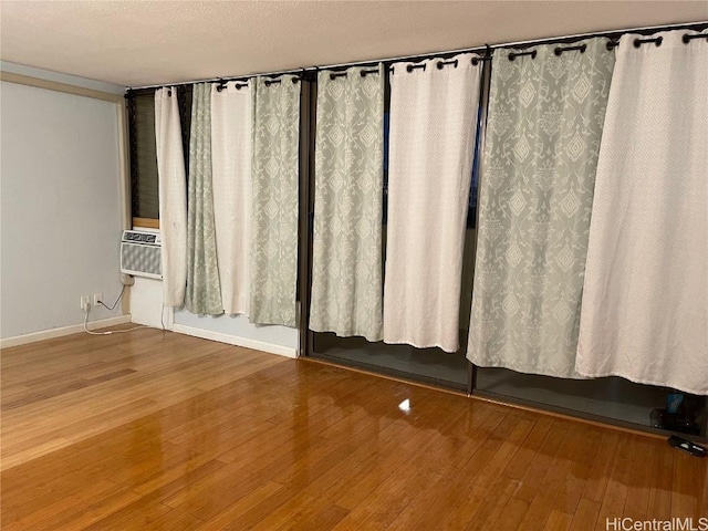 empty room featuring cooling unit, wood finished floors, baseboards, and a textured ceiling