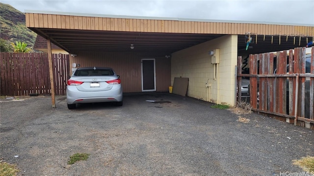 view of car parking with an attached carport, driveway, and fence