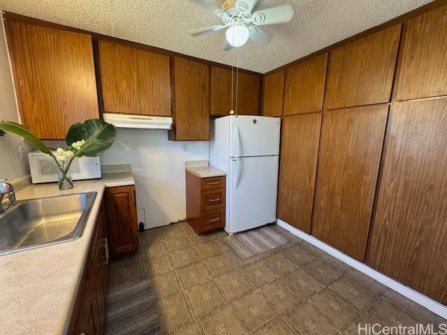 kitchen with white appliances, brown cabinetry, a sink, light countertops, and under cabinet range hood