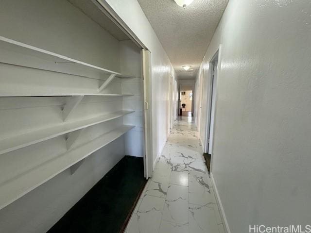 hall with baseboards, a textured ceiling, and marble finish floor