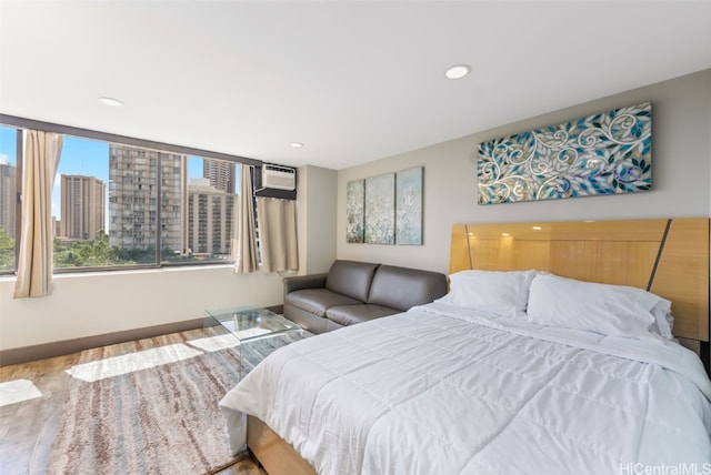 bedroom with a view of city, wood finished floors, a wall unit AC, recessed lighting, and baseboards