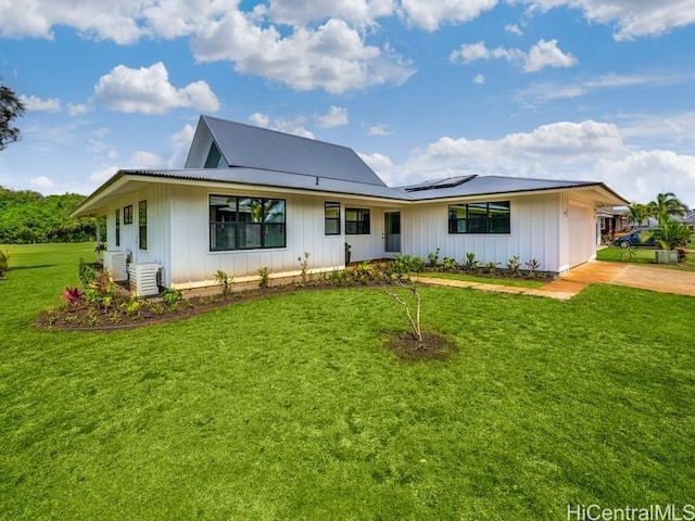 rear view of property with solar panels, board and batten siding, a lawn, a garage, and driveway