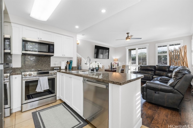 kitchen with a peninsula, a sink, stainless steel appliances, dark countertops, and open floor plan