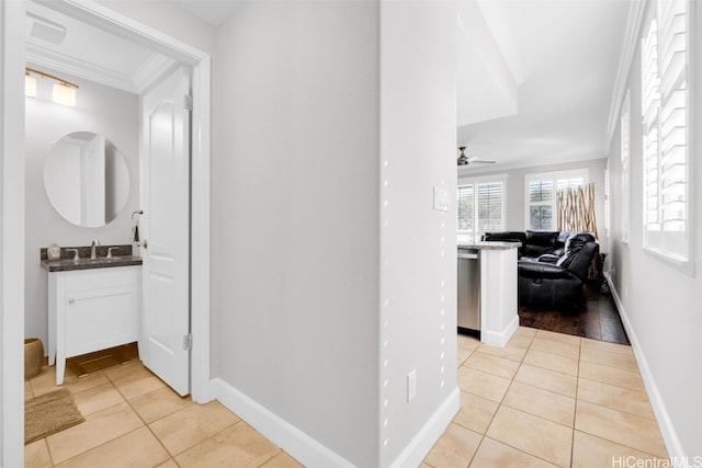 corridor with light tile patterned floors, crown molding, baseboards, and a sink