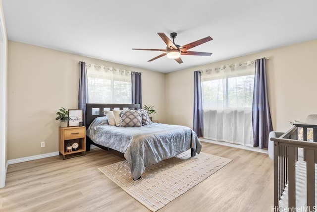 bedroom with multiple windows, light wood-type flooring, baseboards, and ceiling fan