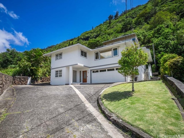 view of front of house featuring stairway, driveway, an attached garage, and a front yard