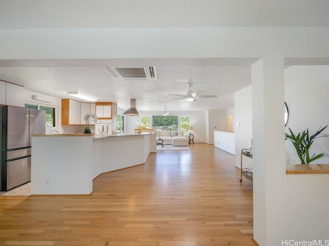 kitchen featuring visible vents, wall chimney range hood, open floor plan, light wood-type flooring, and freestanding refrigerator