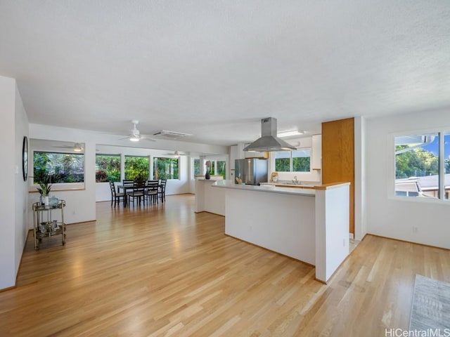 kitchen featuring a healthy amount of sunlight, a peninsula, freestanding refrigerator, light wood-style floors, and island range hood